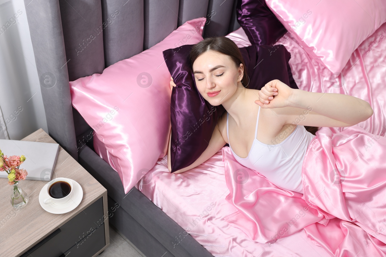 Woman stretching in bed with silk linens indoors Photo of Woman stretching in bed with silk linens indoors