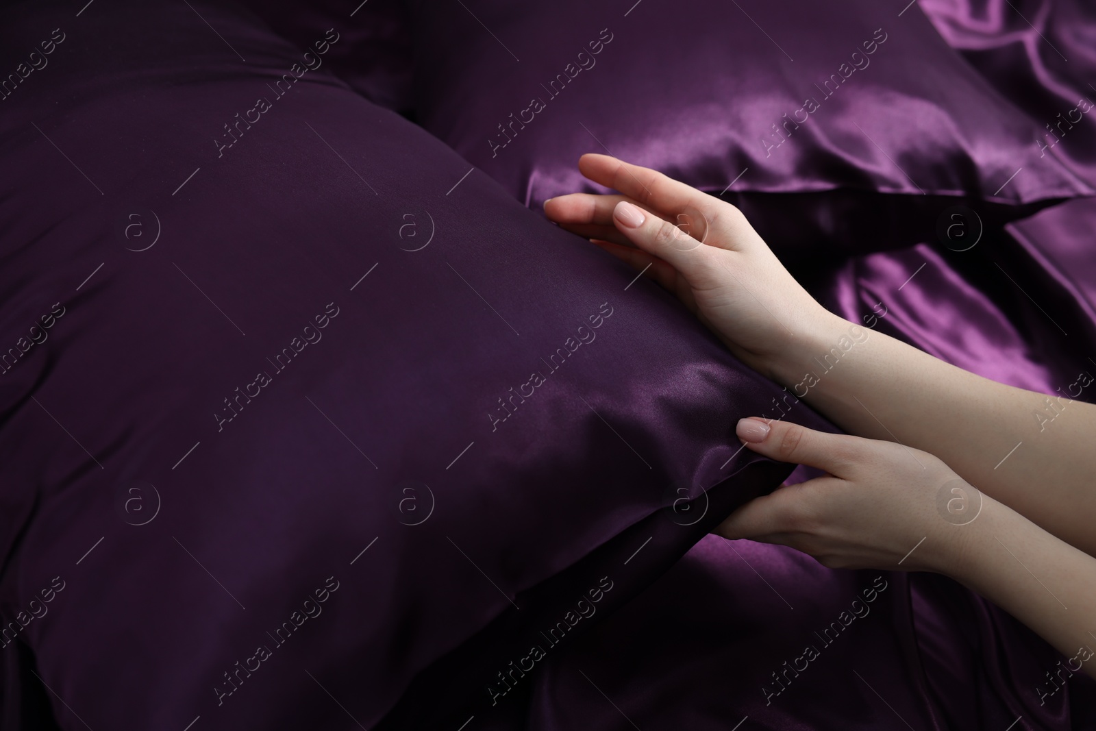 Photo of Woman with pillow on silk bed linens, closeup