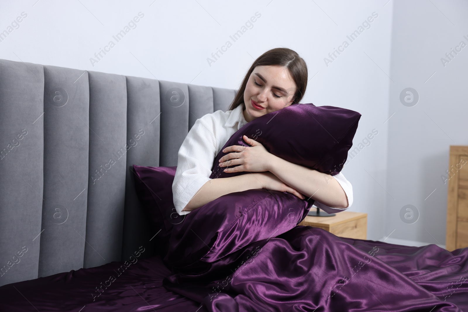 Woman hugging pillow in bed with purple silk linens indoors Photo of Woman hugging pillow in bed with purple silk linens indoors