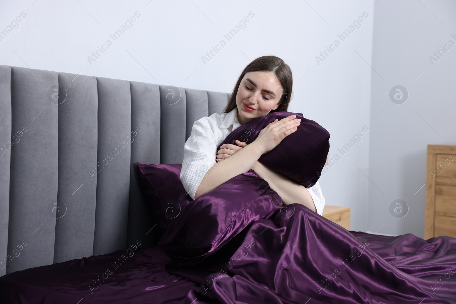 Woman hugging pillow in bed with purple silk linens indoors Photo of Woman hugging pillow in bed with purple silk linens indoors