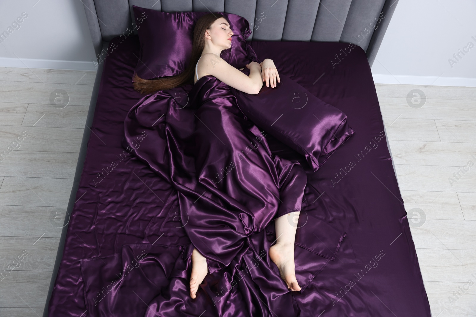 Woman sleeping in bed with purple silk linens indoors, above view Photo of Woman sleeping in bed with purple silk linens indoors, above view