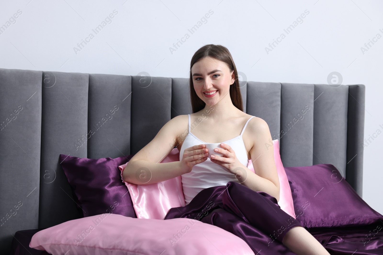Smiling woman drinking coffee in bed with silk linens indoors Photo of Smiling woman drinking coffee in bed with silk linens indoors