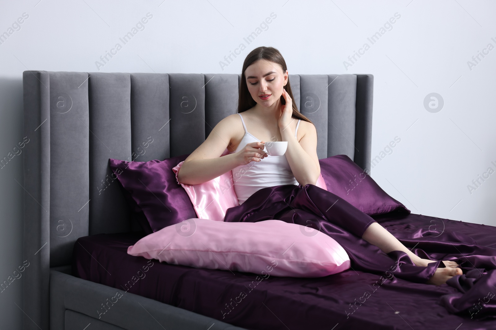 Woman drinking coffee in bed with silk linens indoors Photo of Woman drinking coffee in bed with silk linens indoors