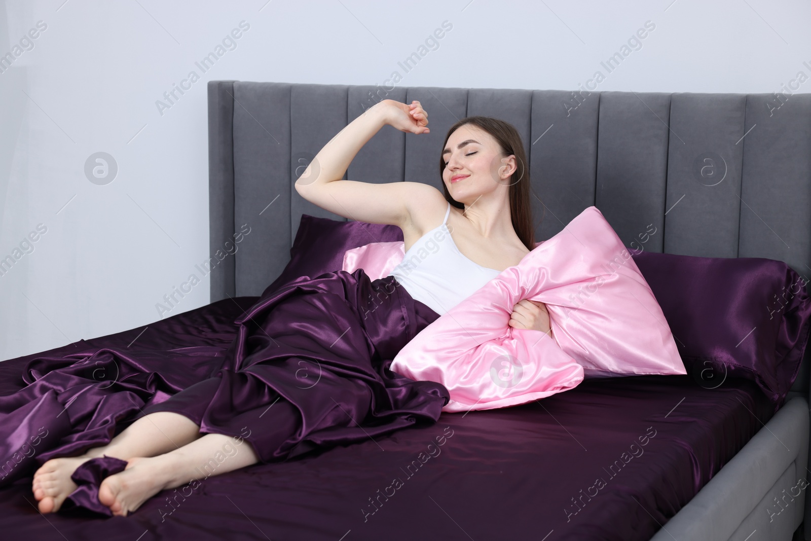Woman stretching in bed with silk linens indoors Photo of Woman stretching in bed with silk linens indoors