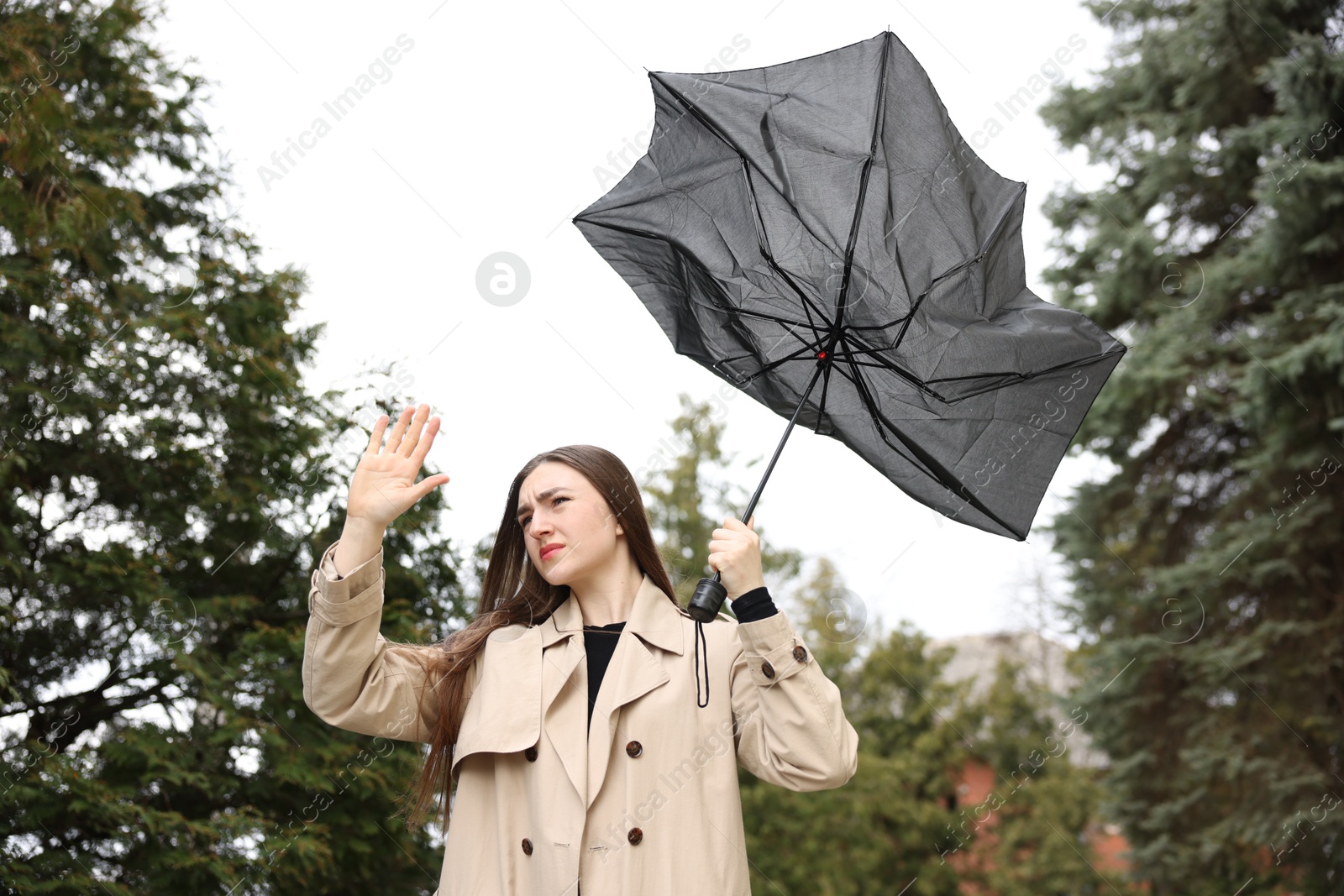 Woman with broken umbrella fighting wind outdoors, low angle view Photo of Woman with broken umbrella fighting wind outdoors, low angle view