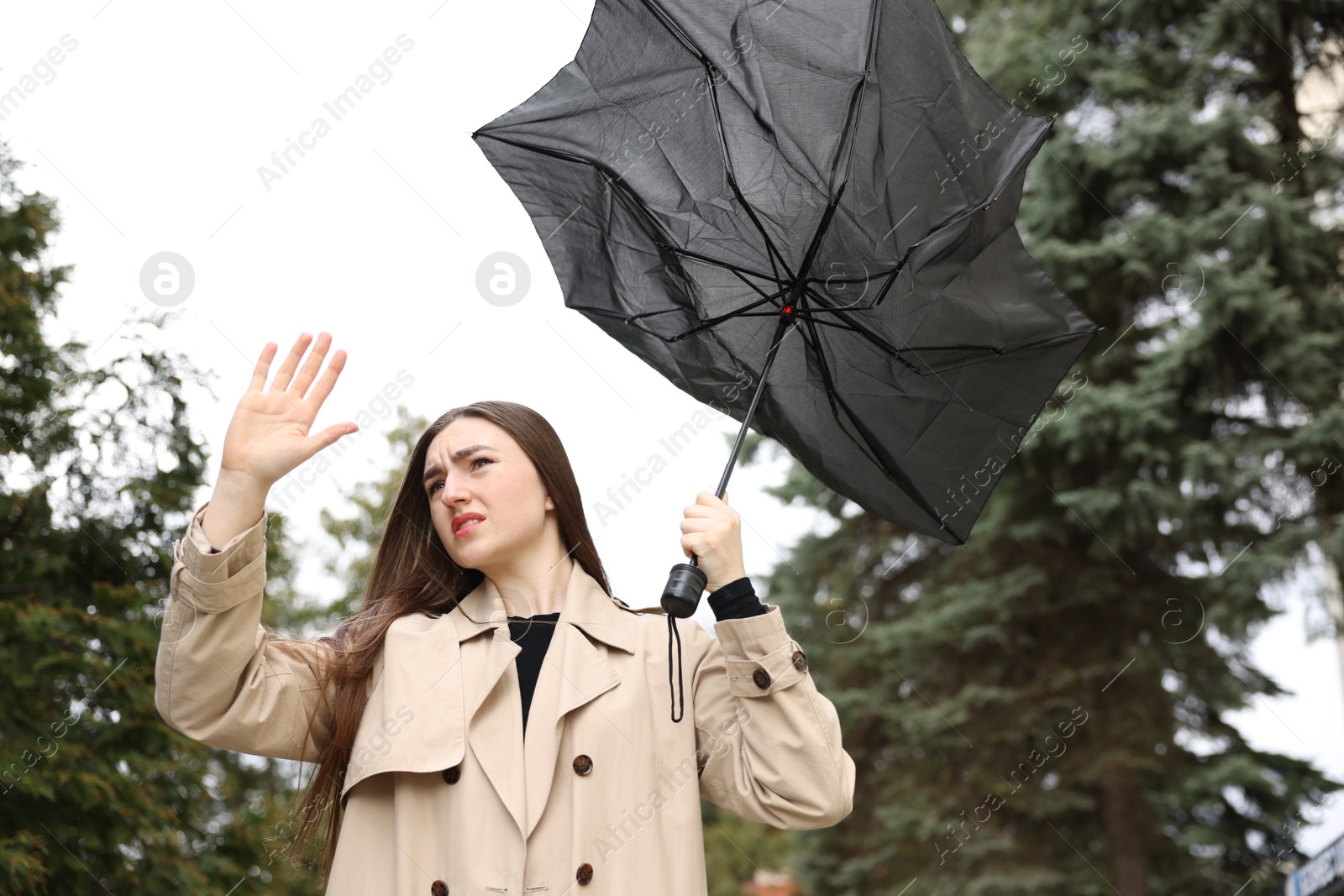 Woman with broken umbrella fighting wind outdoors, low angle view Photo of Woman with broken umbrella fighting wind outdoors, low angle view