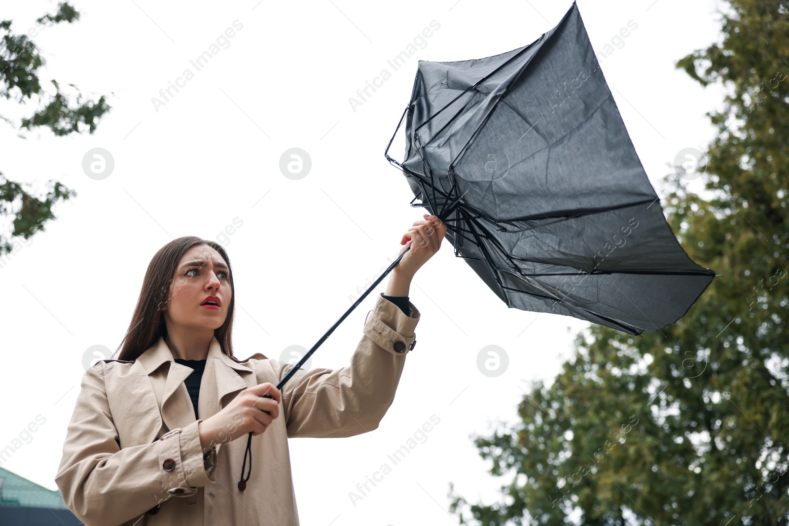 Woman with broken umbrella fighting wind outdoors, low angle view Photo of Woman with broken umbrella fighting wind outdoors, low angle view