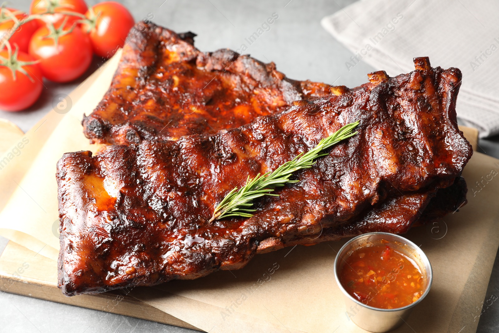 Tasty roasted pork ribs served with rosemary, tomatoes and sauce on light grey table, closeup Photo of Tasty roasted pork ribs served with rosemary, tomatoes and sauce on light grey table, closeup