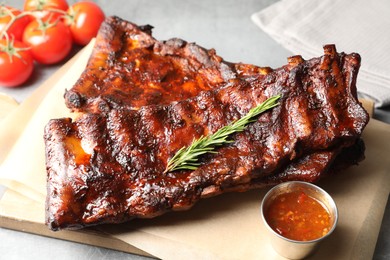 Photo of Tasty roasted pork ribs served with rosemary, tomatoes and sauce on light grey table, closeup