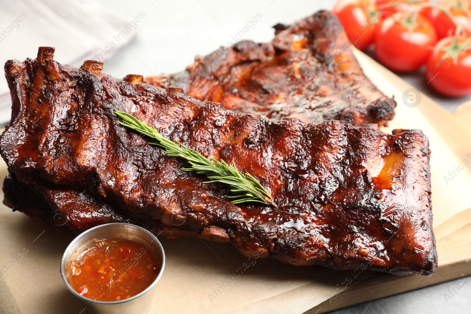 Tasty roasted pork ribs served with rosemary, tomatoes and sauce on light grey table, closeup Photo of Tasty roasted pork ribs served with rosemary, tomatoes and sauce on light grey table, closeup