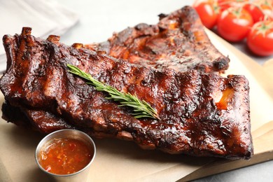 Photo of Tasty roasted pork ribs served with rosemary, tomatoes and sauce on light grey table, closeup