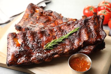 Photo of Tasty roasted pork ribs served with rosemary, tomatoes and sauce on light grey table, closeup