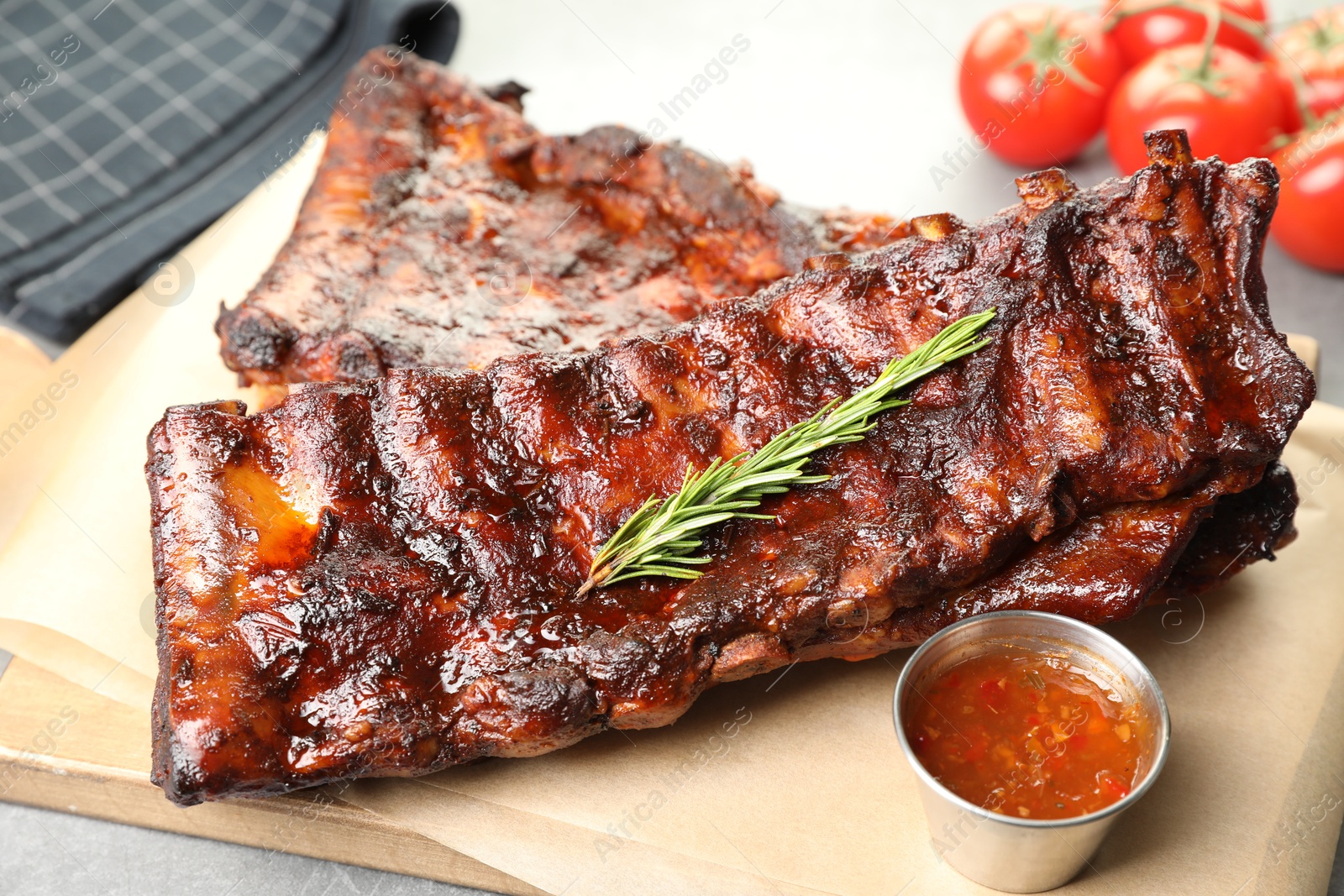 Tasty roasted pork ribs served with rosemary, tomatoes and sauce on light grey table, closeup Photo of Tasty roasted pork ribs served with rosemary, tomatoes and sauce on light grey table, closeup