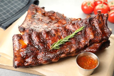 Photo of Tasty roasted pork ribs served with rosemary, tomatoes and sauce on light grey table, closeup