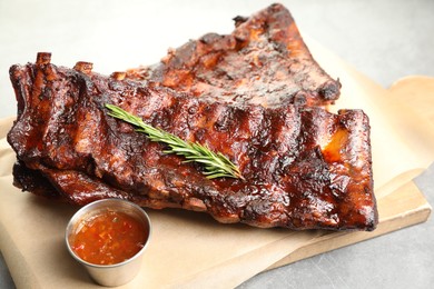 Photo of Tasty roasted pork ribs served with rosemary and sauce on light grey table, closeup