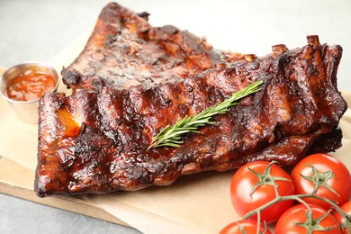 Photo of Tasty roasted pork ribs served with rosemary, tomatoes and sauce on light grey table, closeup