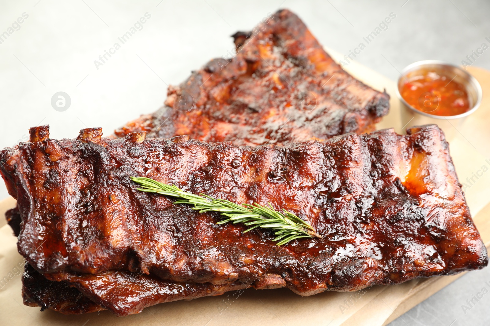 Tasty roasted pork ribs served with rosemary and sauce on light grey table, closeup Photo of Tasty roasted pork ribs served with rosemary and sauce on light grey table, closeup