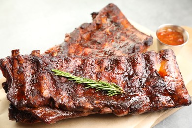Photo of Tasty roasted pork ribs served with rosemary and sauce on light grey table, closeup