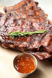 Photo of Tasty roasted pork ribs served with rosemary and sauce on table, closeup