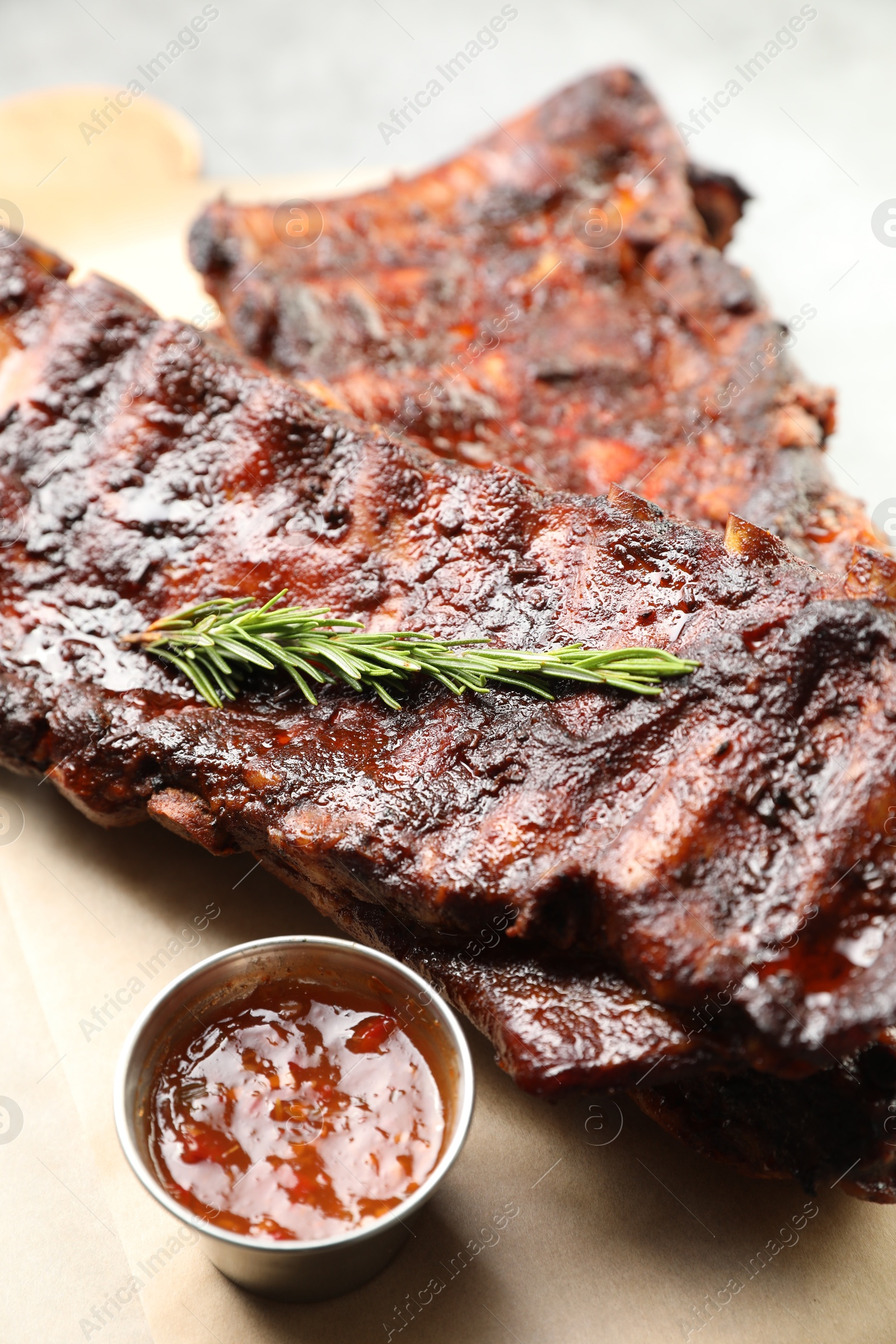 Tasty roasted pork ribs served with rosemary and sauce on table, closeup Photo of Tasty roasted pork ribs served with rosemary and sauce on table, closeup