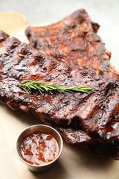 Photo of Tasty roasted pork ribs served with rosemary and sauce on table, closeup
