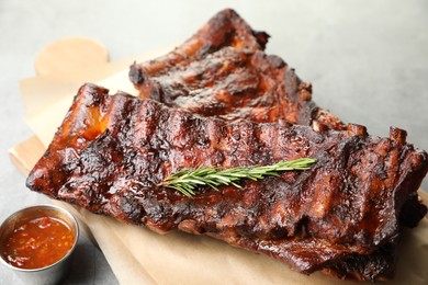 Photo of Tasty roasted pork ribs served with rosemary and sauce on light grey table, closeup