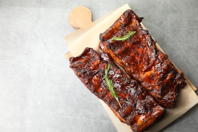 Photo of Tasty roasted pork ribs served with rosemary on light grey table, top view. Space for text