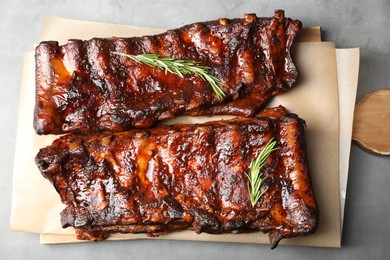 Photo of Tasty roasted pork ribs served with rosemary on light grey table, top view