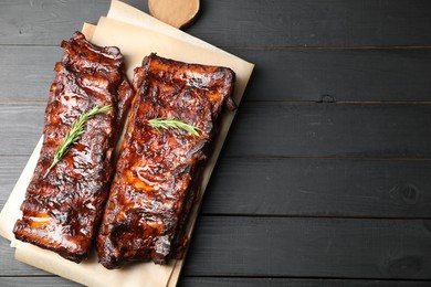 Photo of Tasty roasted pork ribs served with rosemary on black wooden table, top view. Space for text