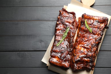 Photo of Tasty roasted pork ribs served with rosemary on black wooden table, top view. Space for text