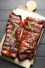 Photo of Tasty roasted pork ribs served with rosemary on black wooden table, top view