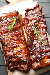 Photo of Tasty roasted pork ribs served with rosemary on black wooden table, top view