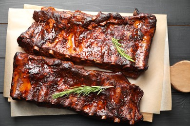 Photo of Tasty roasted pork ribs served with rosemary on black wooden table, top view