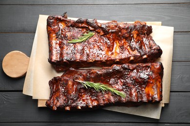 Photo of Tasty roasted pork ribs served with rosemary on black wooden table, top view