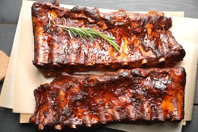 Photo of Tasty roasted pork ribs served with rosemary on black wooden table, top view