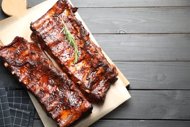 Photo of Tasty roasted pork ribs served with rosemary on black wooden table, top view. Space for text