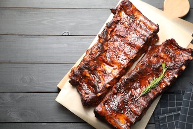 Photo of Tasty roasted pork ribs served with rosemary on black wooden table, top view. Space for text