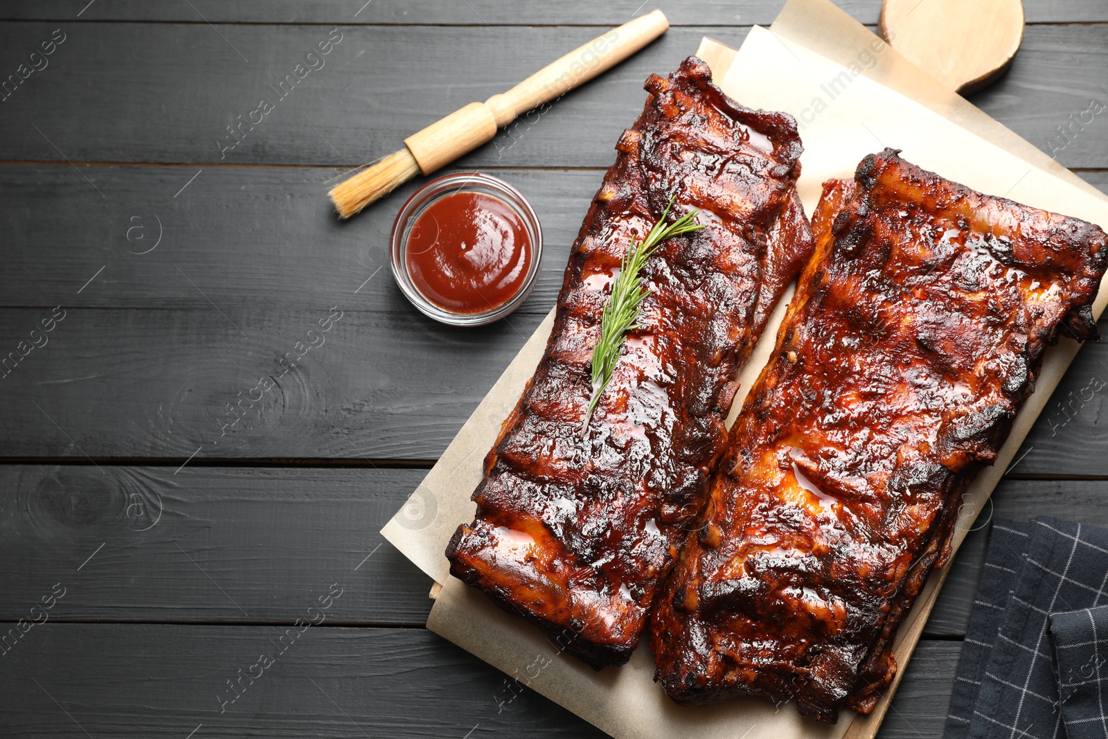 Tasty roasted pork ribs served with rosemary and sauce on black wooden table, flat lay. Space for text Photo of Tasty roasted pork ribs served with rosemary and sauce on black wooden table, flat lay. Space for text