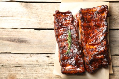 Photo of Tasty roasted pork ribs served with rosemary on wooden table, top view. Space for text