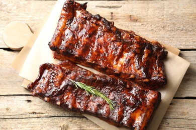 Photo of Tasty roasted pork ribs served with rosemary on wooden table, top view