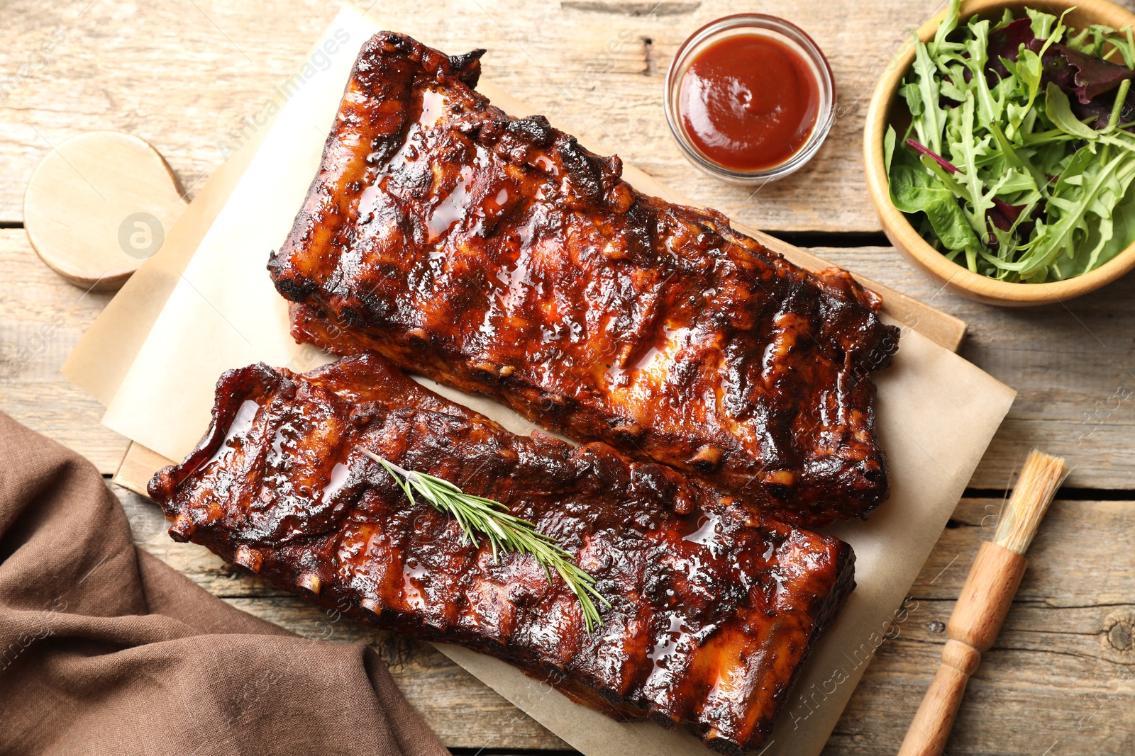 Tasty roasted pork ribs served with rosemary, sauce and salad on wooden table, flat lay Photo of Tasty roasted pork ribs served with rosemary, sauce and salad on wooden table, flat lay