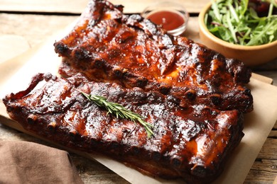 Photo of Tasty roasted pork ribs served with rosemary, sauce and salad on wooden table, closeup