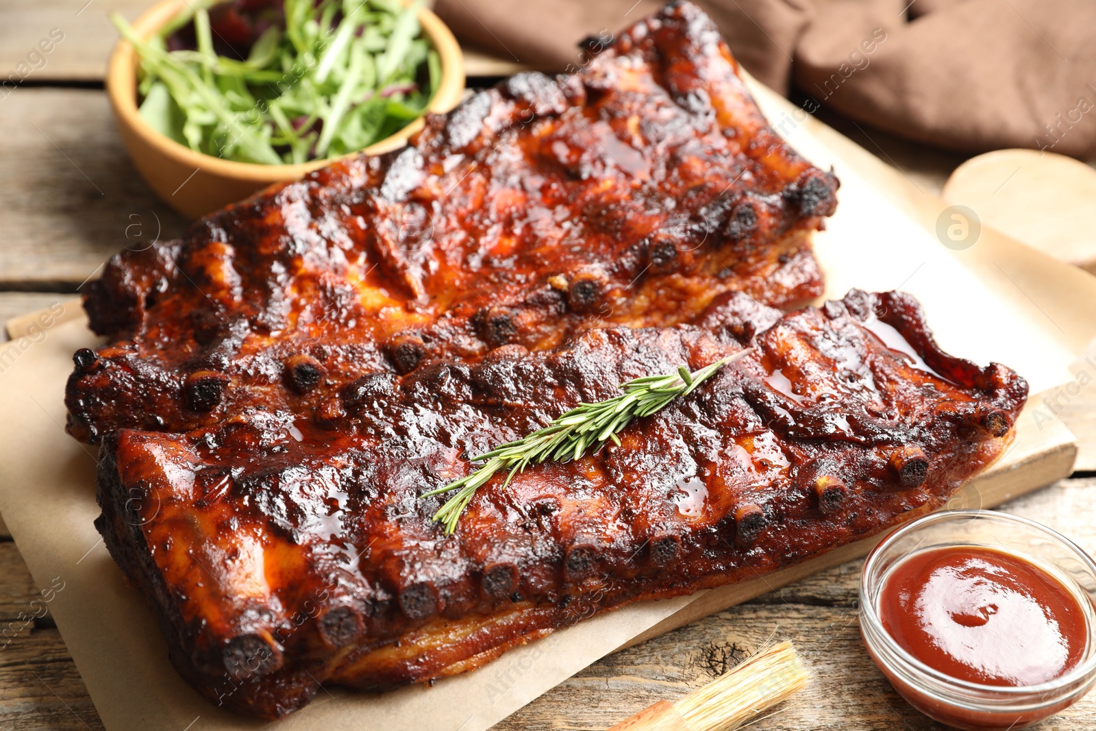 Tasty roasted pork ribs served with rosemary, sauce and salad on wooden table, closeup Photo of Tasty roasted pork ribs served with rosemary, sauce and salad on wooden table, closeup