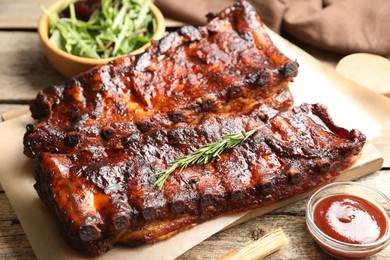 Photo of Tasty roasted pork ribs served with rosemary, sauce and salad on wooden table, closeup