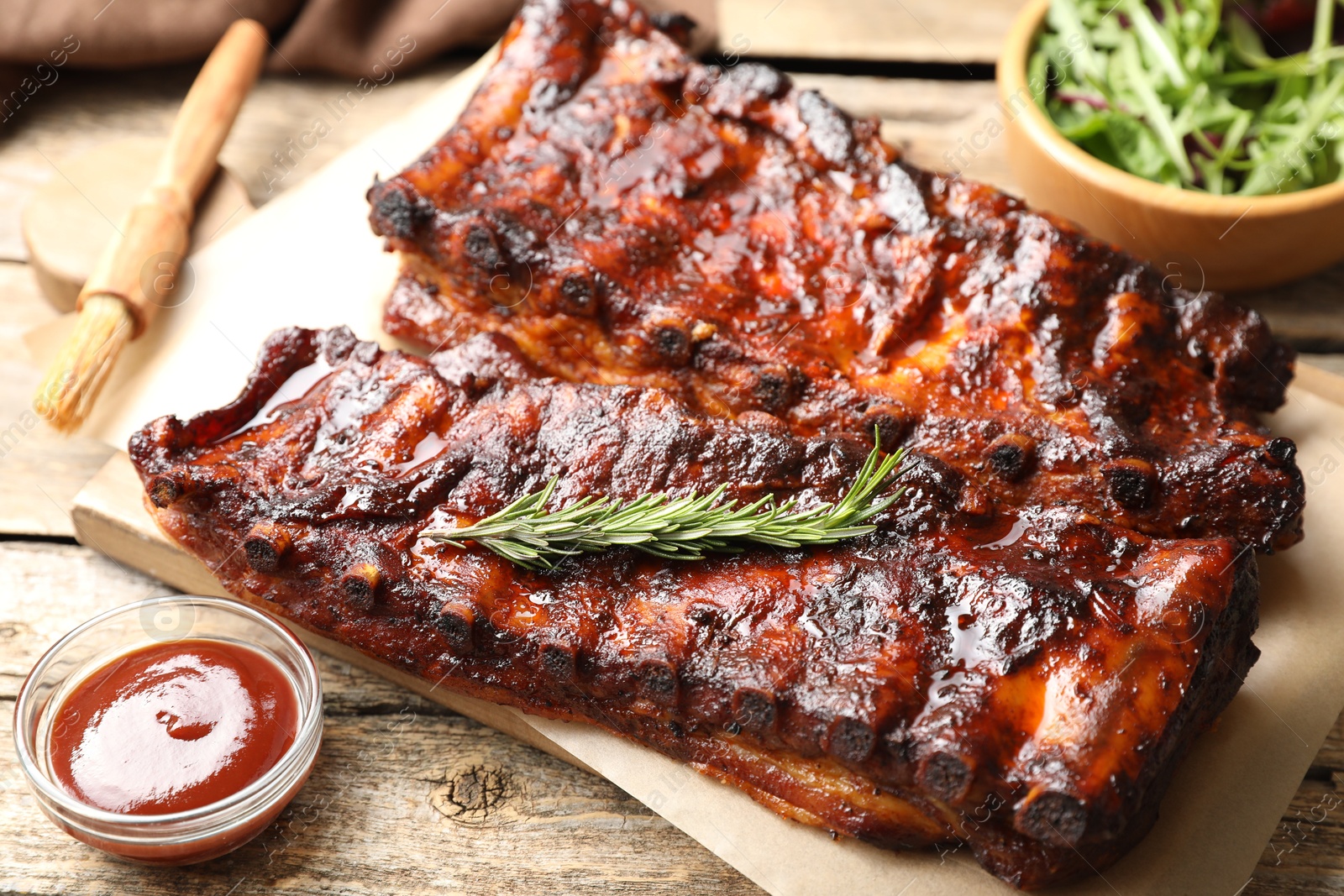 Tasty roasted pork ribs served with rosemary, sauce and salad on wooden table, closeup Photo of Tasty roasted pork ribs served with rosemary, sauce and salad on wooden table, closeup