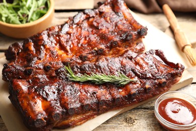 Photo of Tasty roasted pork ribs served with rosemary, sauce and salad on wooden table, closeup