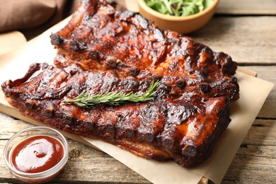 Photo of Tasty roasted pork ribs served with rosemary, sauce and salad on wooden table, closeup