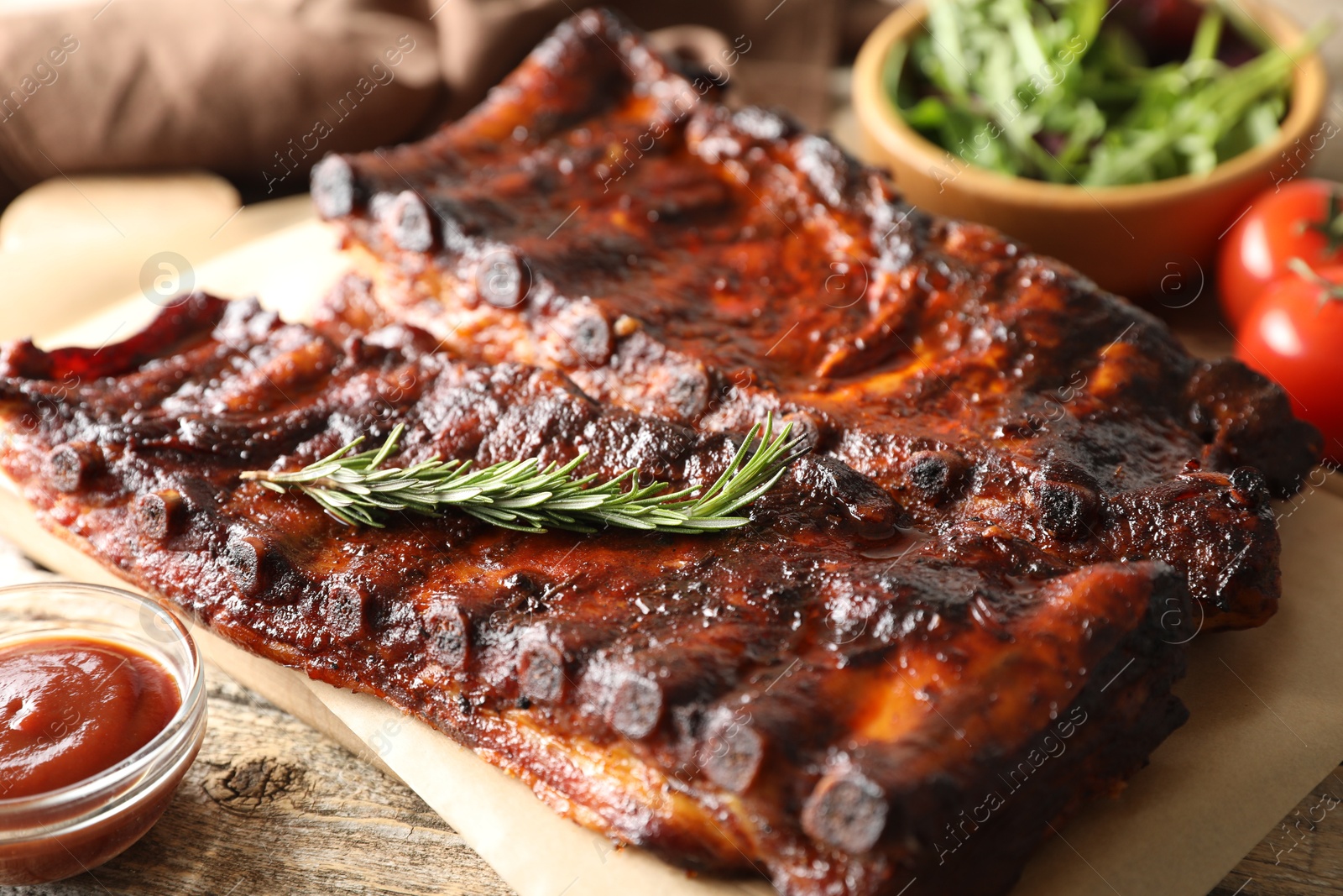 Tasty roasted pork ribs served with rosemary, sauce and salad on wooden table, closeup Photo of Tasty roasted pork ribs served with rosemary, sauce and salad on wooden table, closeup