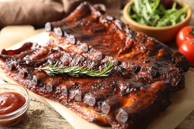 Photo of Tasty roasted pork ribs served with rosemary, sauce and salad on wooden table, closeup