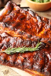 Photo of Tasty roasted pork ribs served with rosemary on wooden table, closeup